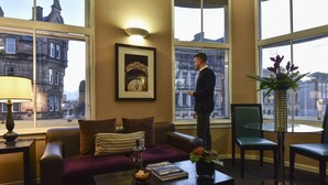 Een hotelkamer met een groot raam, een bank, een bijzettafeltje en een stoel.