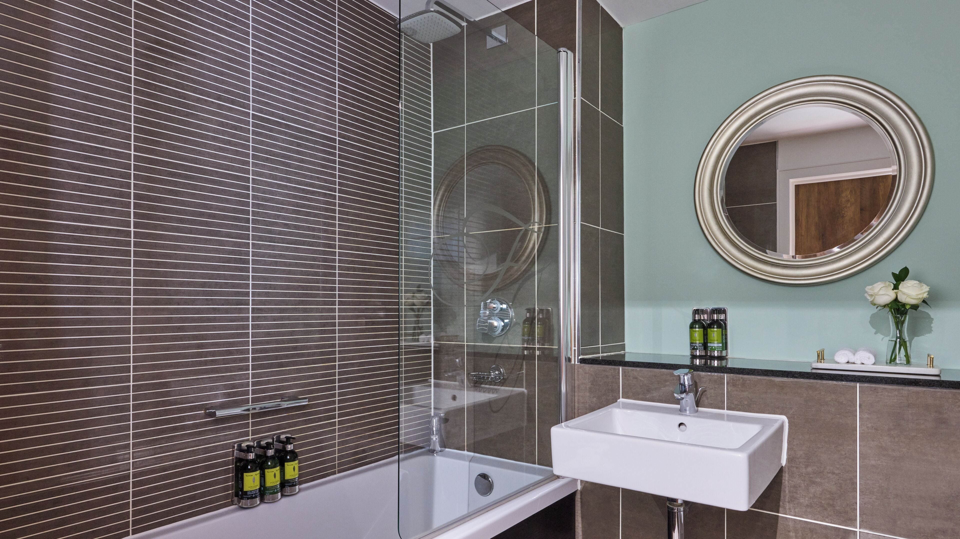 A modern bathroom with a glass-enclosed shower, a white sink, and a mirror with a gold frame.