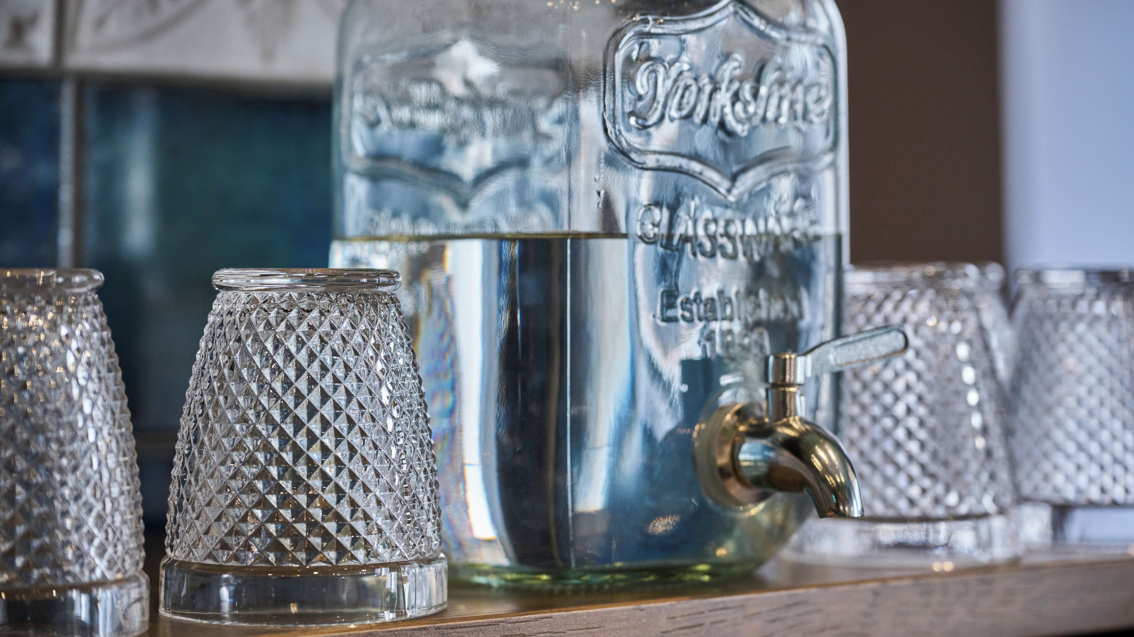 A collection of clear glassware on a shelf, including a large bottle and several glasses with textured patterns.
