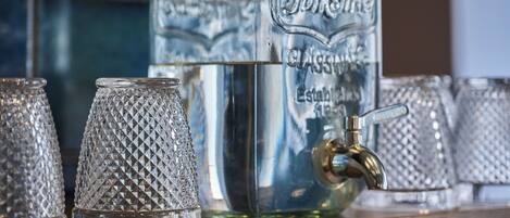 Une collection de verres transparents disposés sur une étagère, comprenant une grande bouteille et plusieurs verres ornés de motifs en relief.