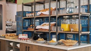 Een ontbijtbuffet met diverse soorten eten, zoals brood, gebak en ontbijlgranen, evenals een koffieapparaat en sapautomaten.