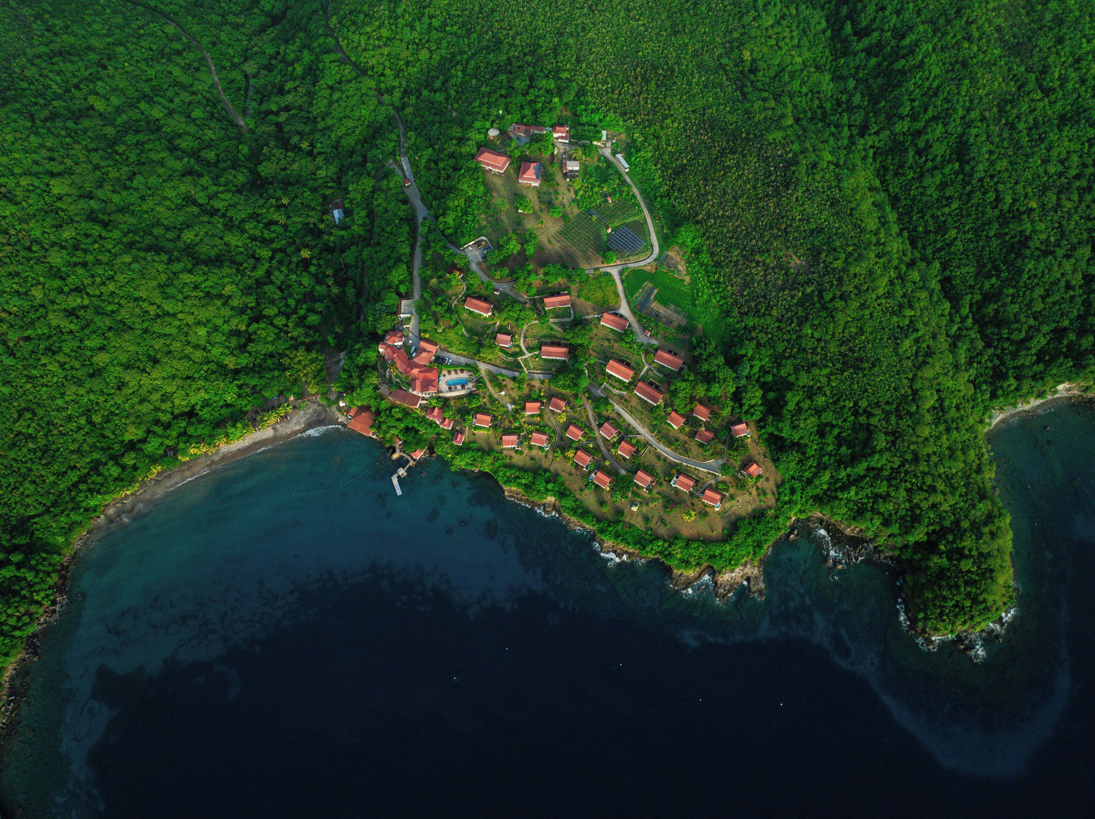 Luftaufnahme eines Küstenresorts mit mehreren Gebäuden mit roten Dächern, einem Schwimmbad und einem kleinen Jachthafen.