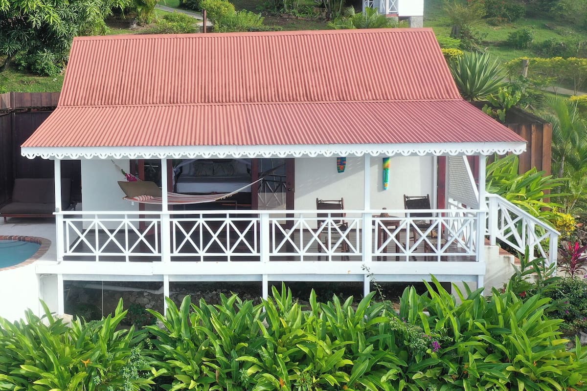 A two-story house with a red roof, a balcony with white railings, and a swimming pool.