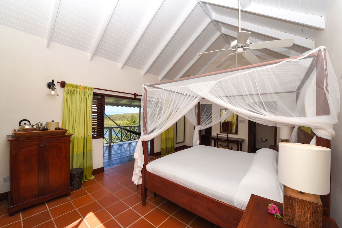 A bedroom with a wooden bed, a nightstand, a lamp, a wooden cabinet, a window with a view, and a ceiling fan.