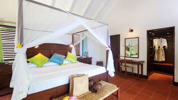 A bedroom with a canopy bed, colorful pillows, a bedside table, a mirror, a wooden bench, and a wardrobe.