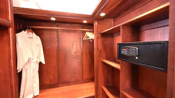 Un armario vestidor de madera con bata colgada, estantes de madera y una caja fuerte electrónica negra.
