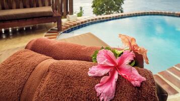 A poolside area with a wooden fence, a lounge chair, and towels with a hibiscus flower.