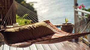 Een hangstoel met een bruin kussen op een houten terras, met uitzicht op de zee.