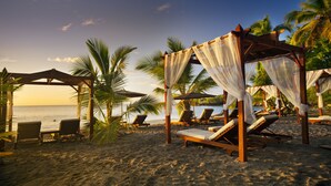 Een strand met houten cabana's, palmbomen en ligstoelen.