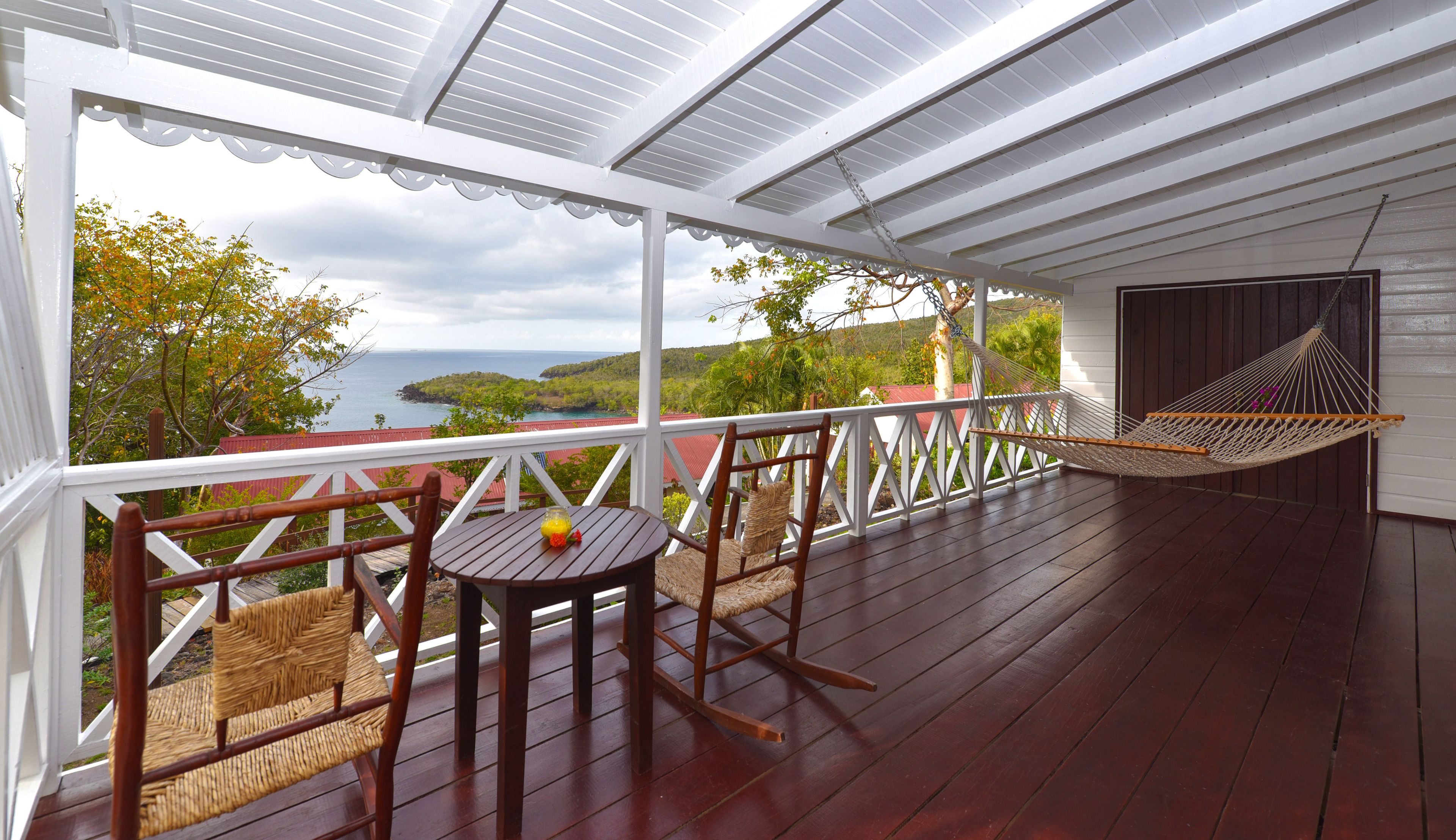 Un espace extérieur abrité, doté d’une terrasse en bois, d’un hamac, d’une table avec un verre de jus de fruits et de chaises.