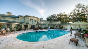 A swimming pool with lounge chairs and umbrellas, surrounded by a building with a tiled patio.