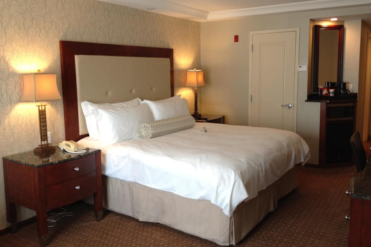 Une chambre d’hôtel avec un grand lit, deux tables de chevet avec des lampes, une commode, un miroir et une porte.