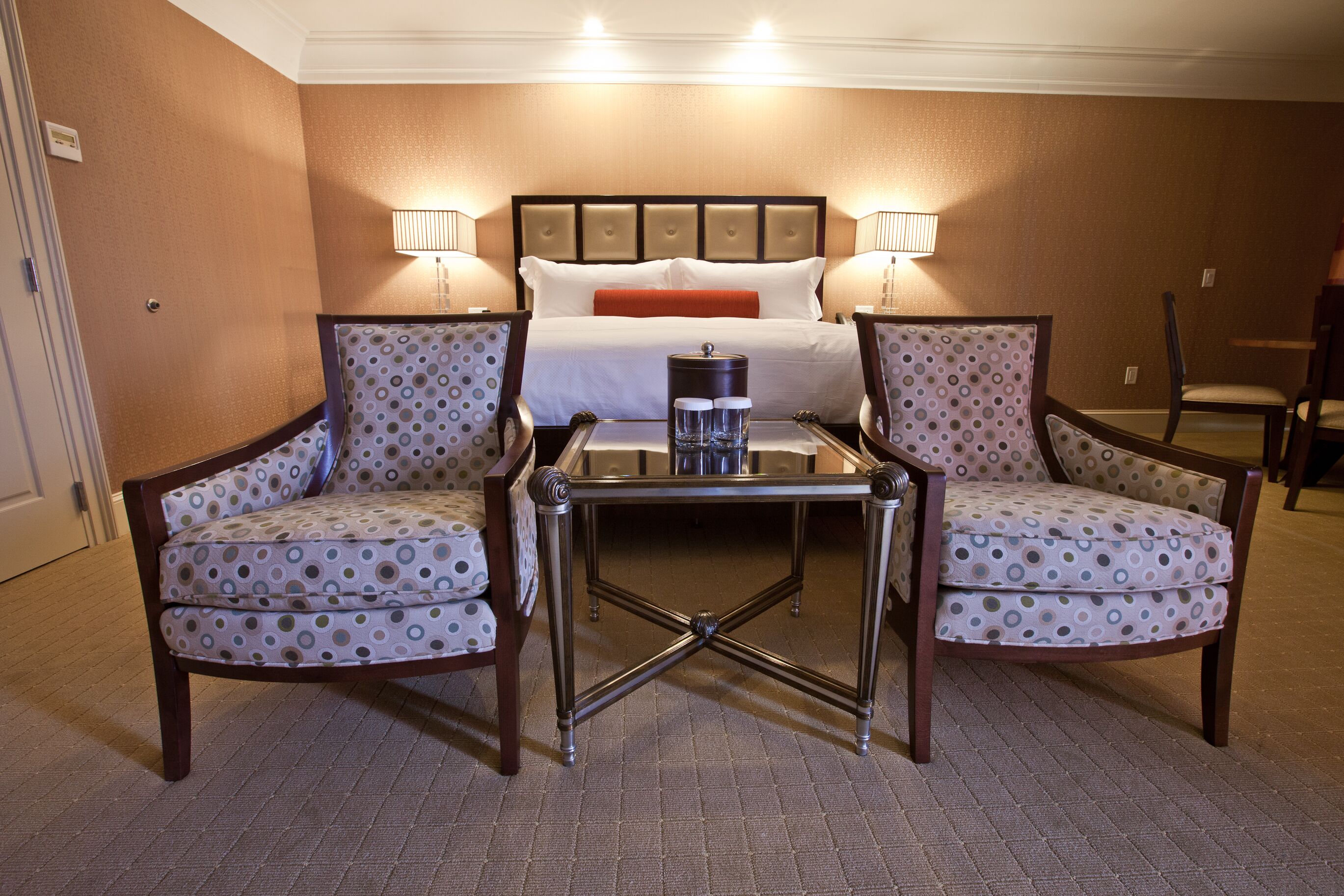 Una habitación de hotel con una cama, dos sillones, una mesita y dos lámparas de noche.