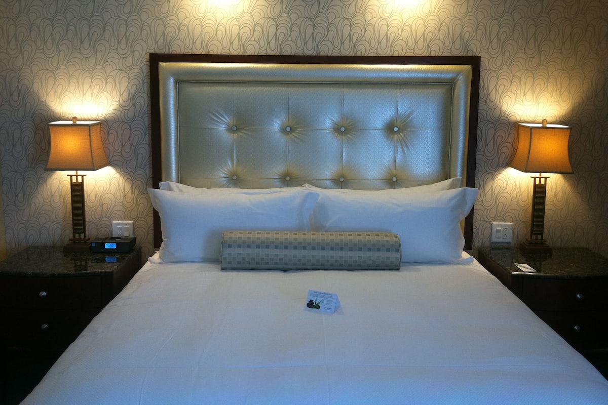 Une chambre d’hôtel avec un grand lit, deux lampes de chevet, une horloge murale et une tête de lit décorative.