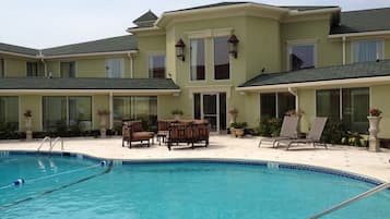 A pool area with lounge chairs and a building with large windows and a covered patio.