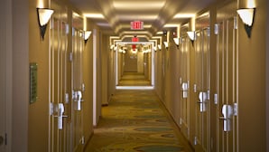 A hotel hallway with multiple doors, illuminated exit signs, and a patterned carpet.