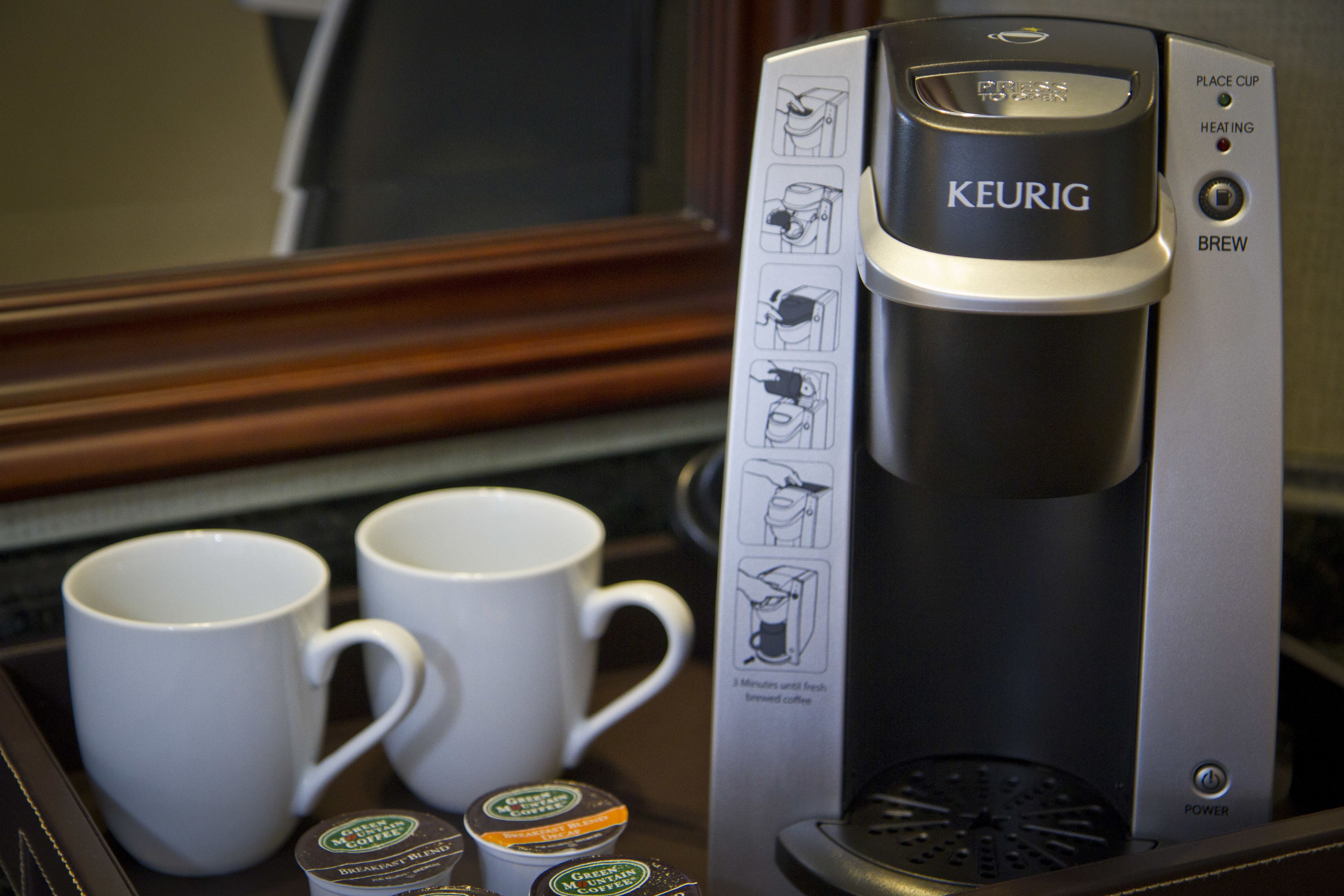 Una cafetera Keurig con dos tazas blancas y cápsulas de café sobre una bandeja.