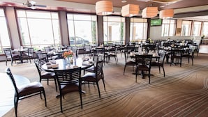 A spacious dining area with multiple tables and chairs, large windows, and hanging pendant lights.
