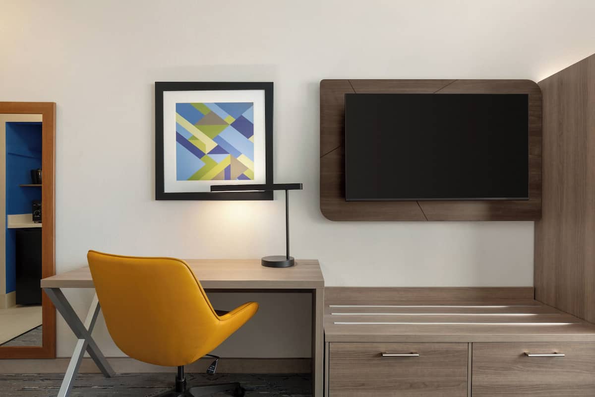 A modern room with a desk, a yellow chair, a framed abstract artwork, a flat-screen TV, and wooden cabinetry.