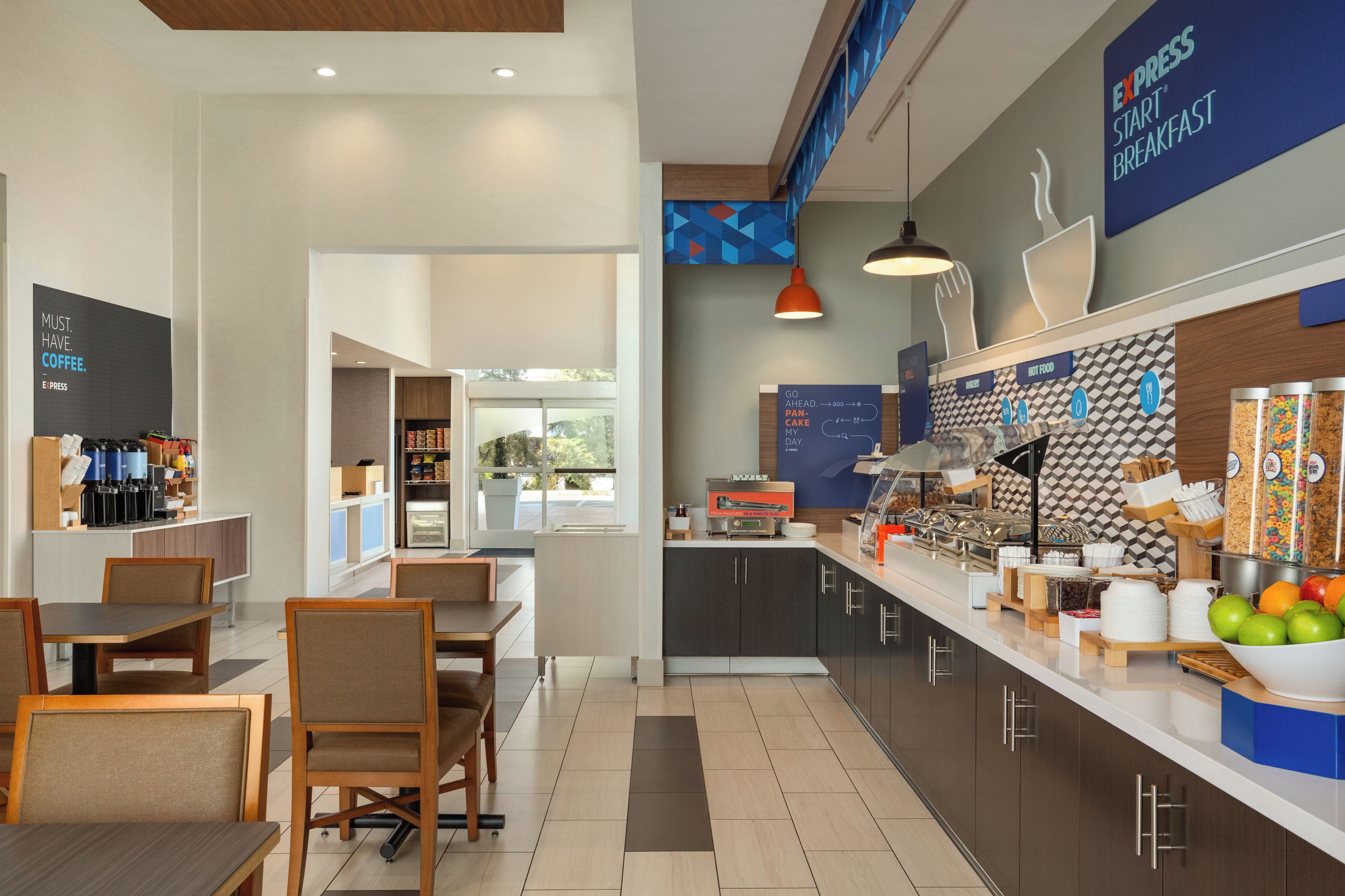 Un espace moderne dédié au petit-déjeuner, comprenant un coin café, des sièges et un comptoir où sont proposés différents plats.