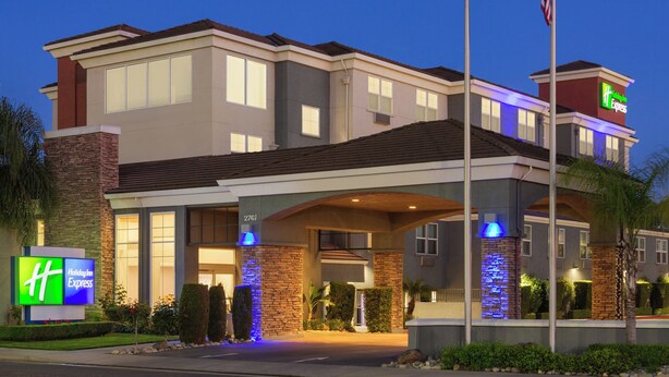 A Holiday Inn Express hotel with a modern design, featuring a prominent entrance with a covered walkway, a brick facade, and an American flag on a flagpole. - Holiday Inn Express West Sacramento by IHG (West Sacramento)