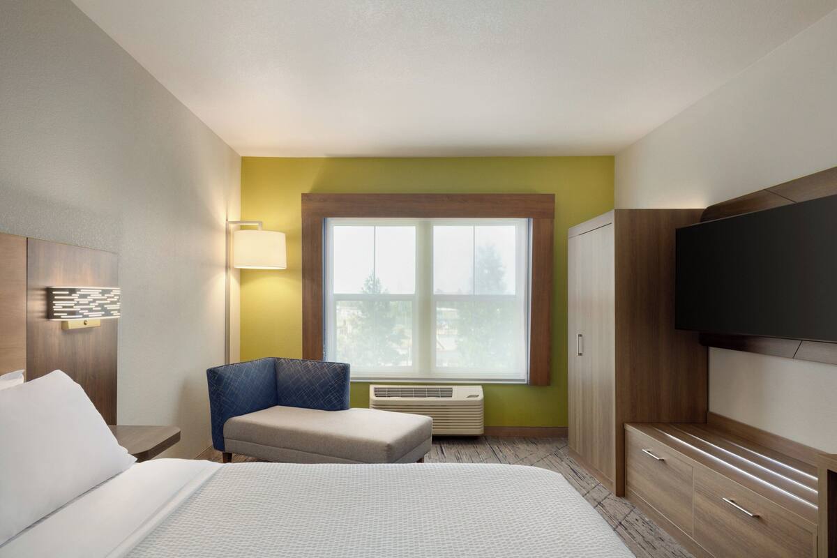 A hotel room with a bed, a chair, a desk, a TV, and a window.