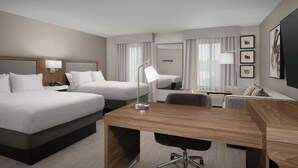 Quarto de hotel com duas camas, uma escrivaninha, uma cadeira, um abajur, um espelho e uma televisão.