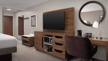 A hotel room with a bed, a desk with a flat-screen TV, a mirror, a lamp, and a microwave.
