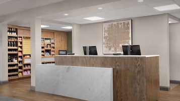 A hotel reception desk with a wooden finish and a marble counter, flanked by shelves stocked with various items.