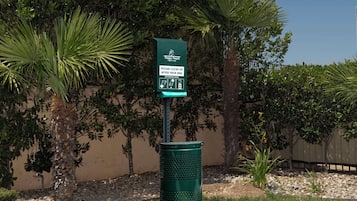 A green trash can with a sign instructing to clean up after your dog and dispose of waste.