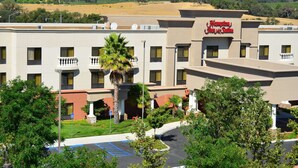 Um hotel com uma placa indicando "Hampton Inn & Suites", rodeado por vegetação e um estacionamento.
