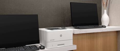 Un bureau moderne équipé d’un ordinateur de bureau, d’un ordinateur portable et d’une imprimante HP, le tout posé sur un bureau blanc devant un mur gris.