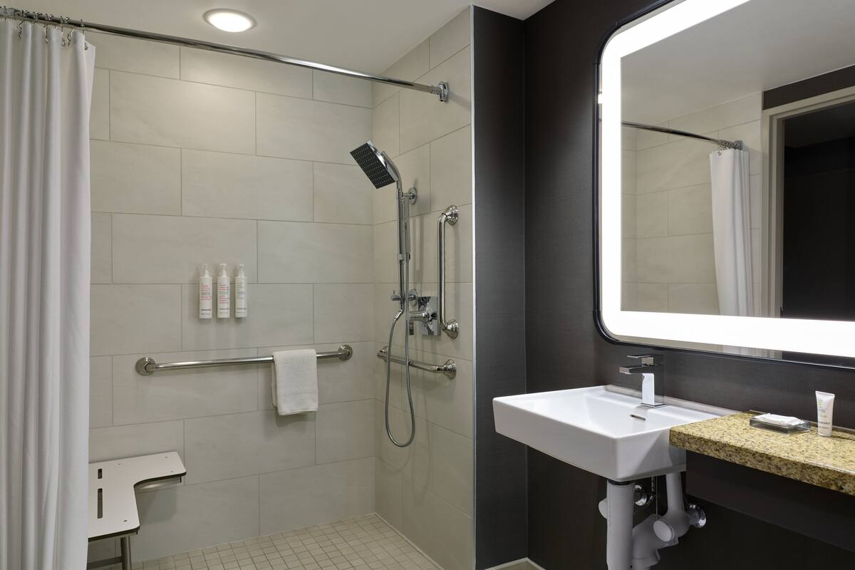 Un baño moderno con cabina de ducha, barras de apoyo, un lavabo blanco y un espejo grande.