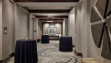A hotel corridor with three round tables, a patterned carpet, and a framed artwork on the wall.