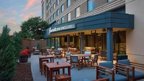An outdoor seating area with wooden tables and chairs, a wine bar & grill sign, and a building with large windows. - Marriott Denver South at Park Meadows (Lone Tree)