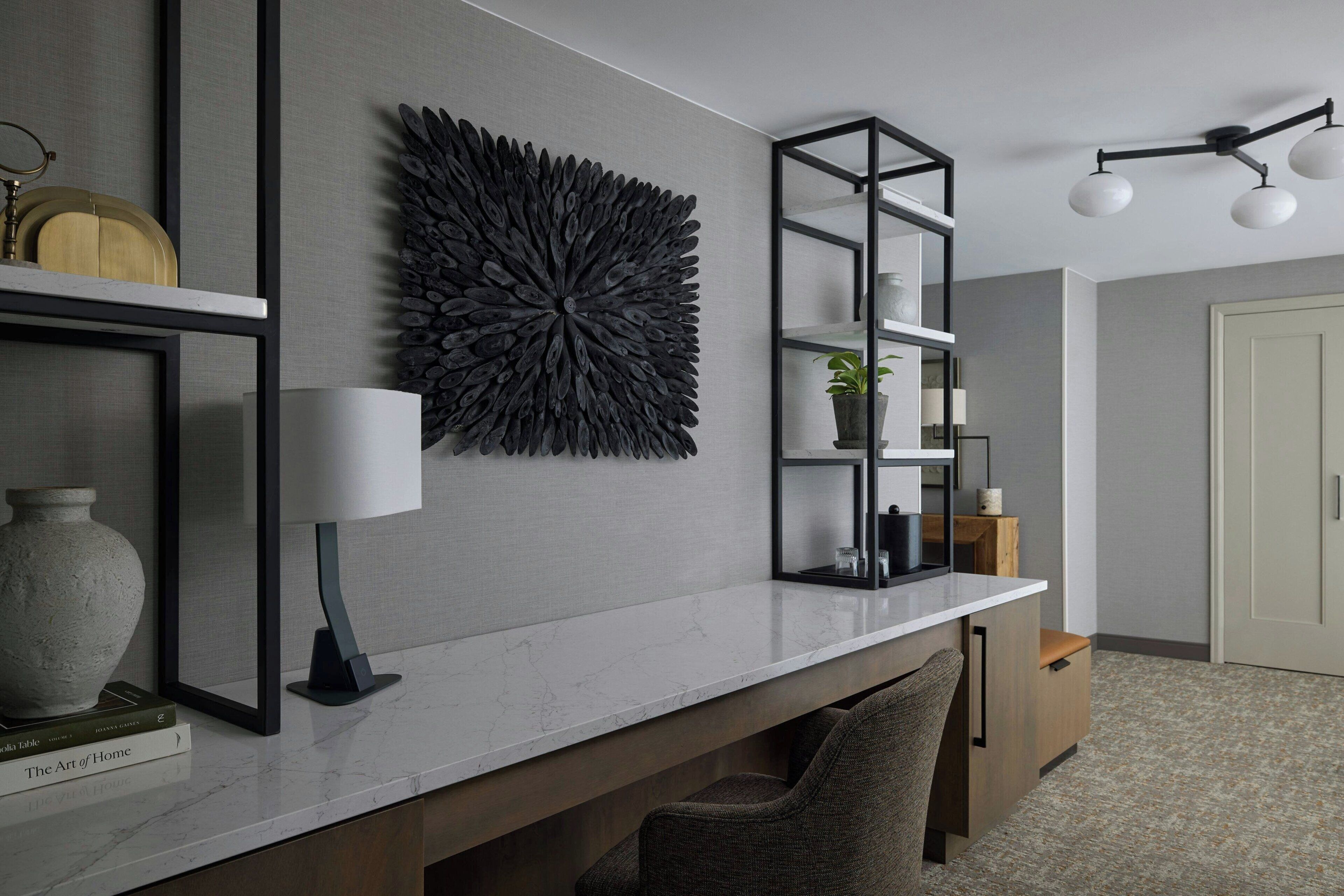 Ein modernes Interieur mit Marmorarbeitsplatte, einer Wanddekoration, einem schwarzen Regalsystem und einer Deckenleuchte.