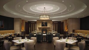 A restaurant with a central fireplace, multiple tables, and chairs arranged for dining. - Marriott Denver South at Park Meadows (Lone Tree)