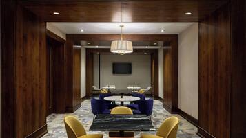 A conference room with a round table, yellow chairs, a black table, blue upholstered chairs, and a hanging light fixture.