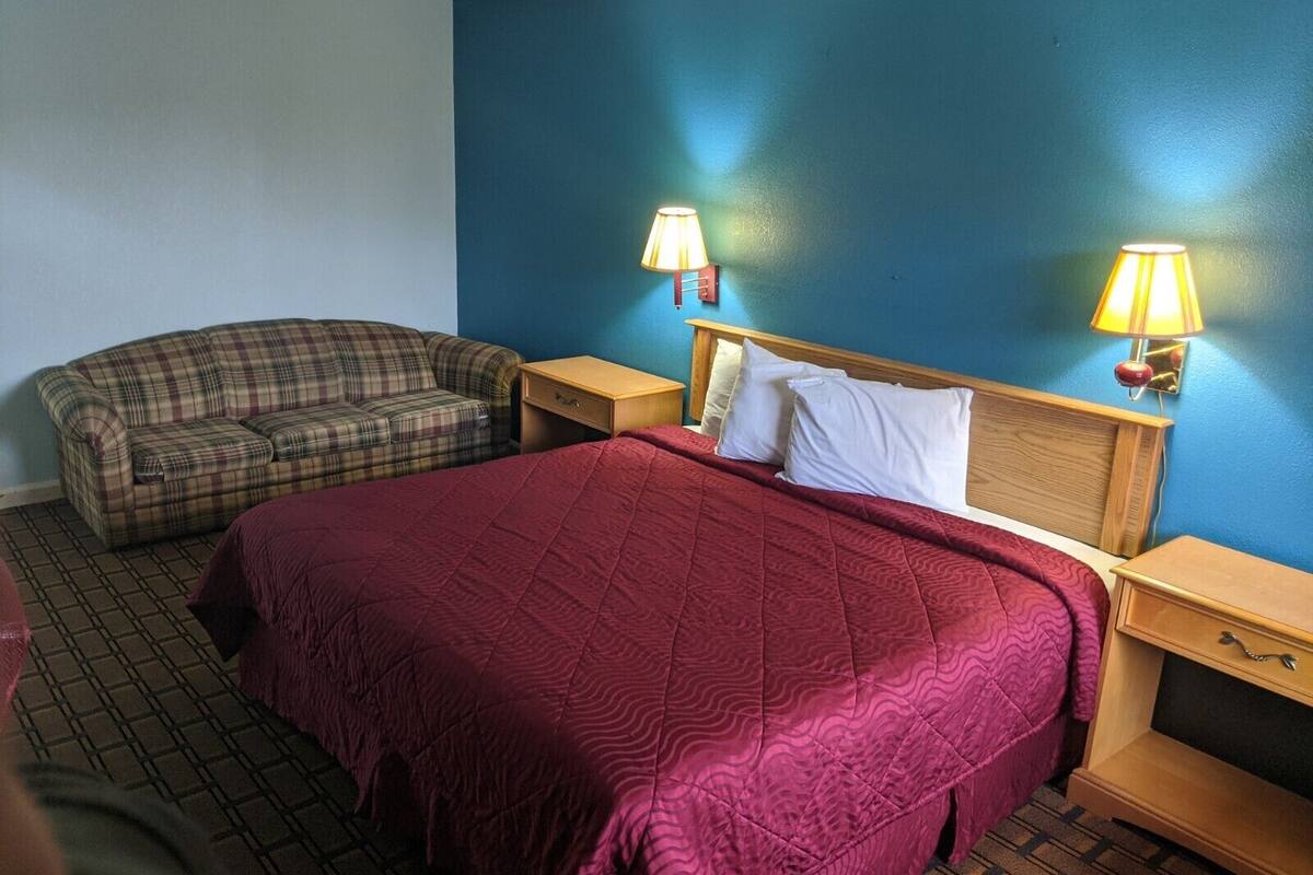 A hotel room with a large bed, a plaid sofa, two bedside tables with lamps, and a blue accent wall.