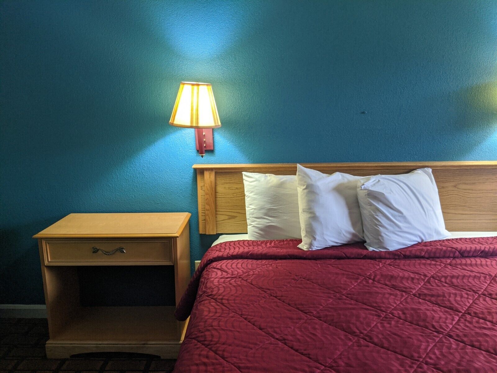 Una habitación de hotel con una cama, una mesita de noche y una lámpara de pared.