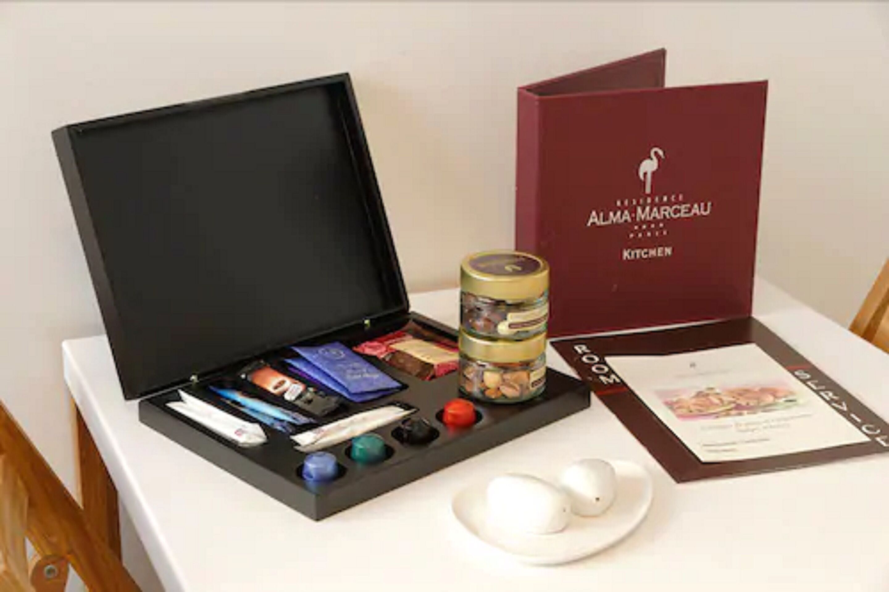 A black gift box with chocolates, a jar of nuts, and a card on a table.