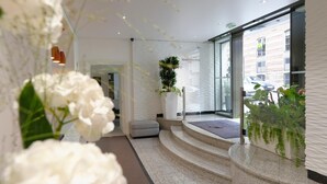A modern hotel lobby with a glass entrance, a staircase leading to a seating area, and indoor plants. - Résidence Alma Marceau (Paris)