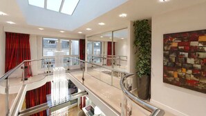 A modern interior with a glass staircase, a large window, and a plant. - Résidence Alma Marceau (Paris)