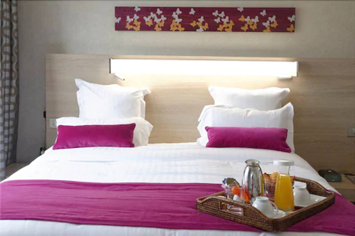 Habitación de hotel con una cama, dos almohadas, una bandeja con alimentos para el desayuno y una obra de arte en la pared.