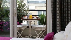 A balcony with a table set for breakfast, two chairs, and a view of the city. - Résidence Alma Marceau (Paris)