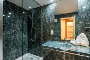 Un baño moderno con un lavamanos de vidrio, ducha y pared de mármol.