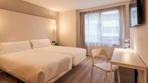Een hotelkamer met twee bedden, een bureau, een stoel, een televisie en een raam met gordijnen.