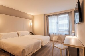 Habitación de hotel con dos camas, un escritorio, una silla, un televisor y una ventana con cortinas.