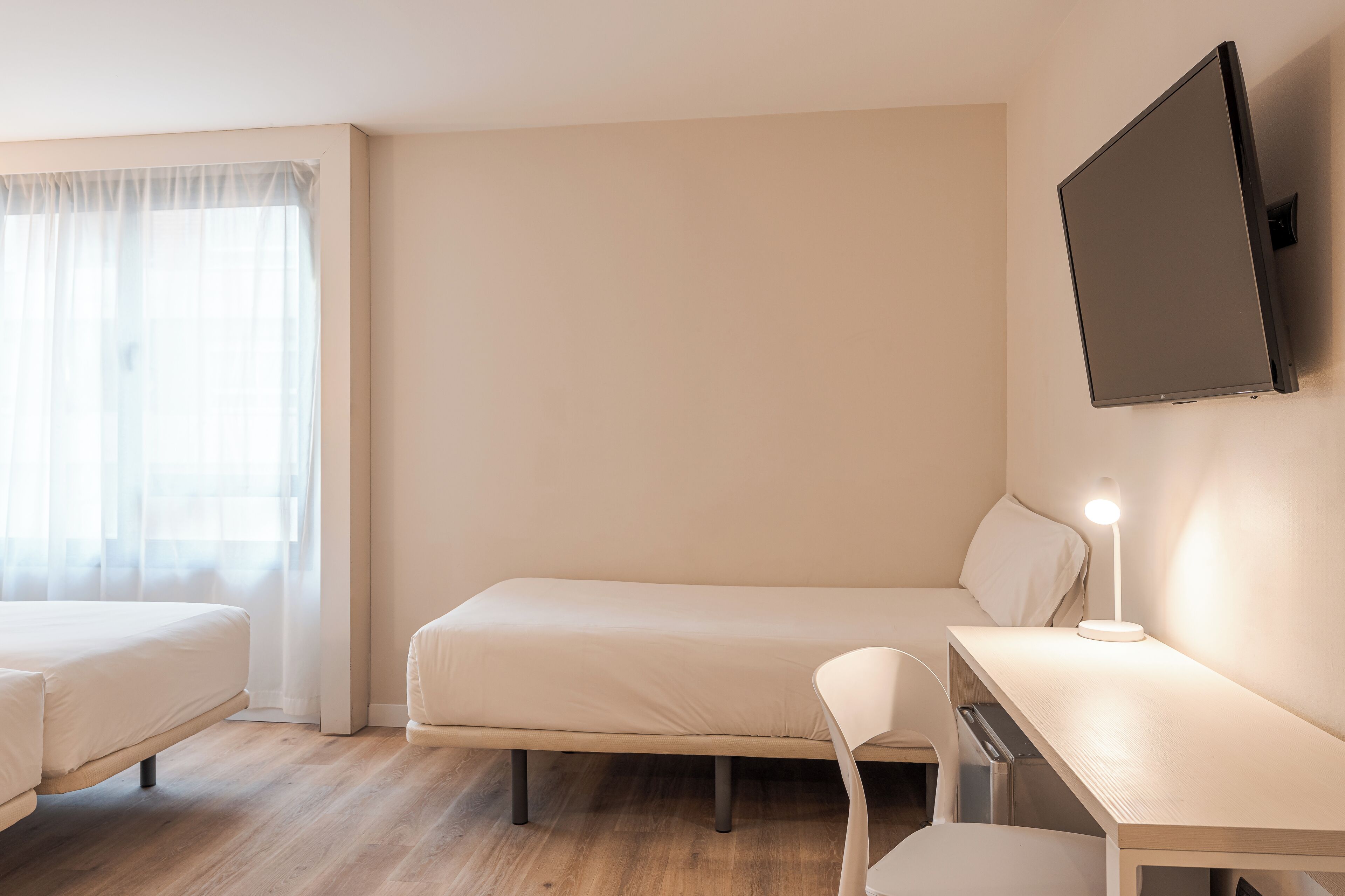 Habitación de hotel con dos camas, un escritorio con lámpara y un televisor instalado en la pared.