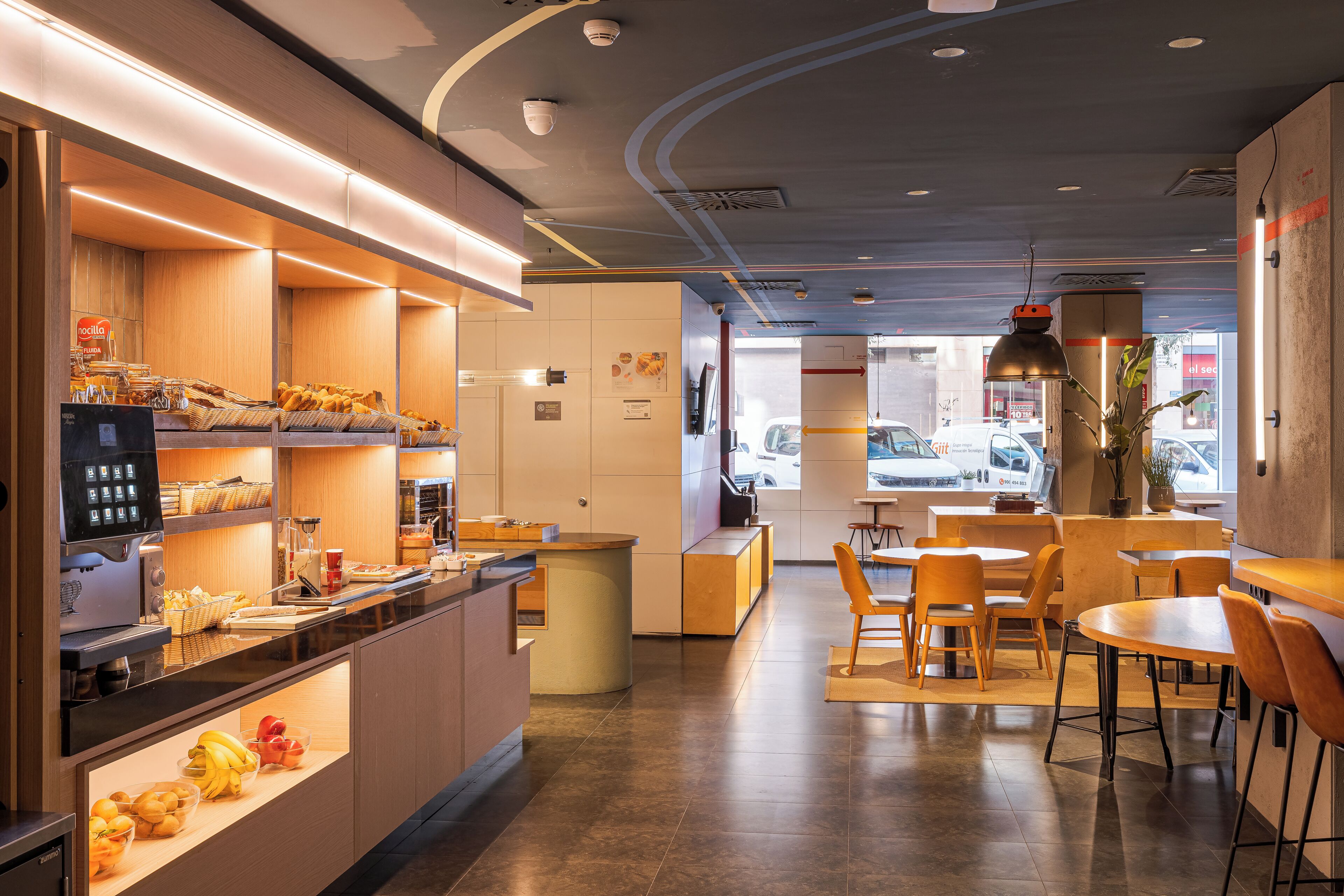 L'intérieur d'un café moderne, avec un comptoir, un espace salon et une vue sur la rue.